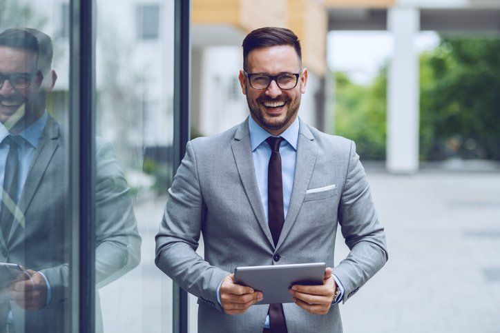 A happy travel agent in a suit an tie holding an iPad walking down the street