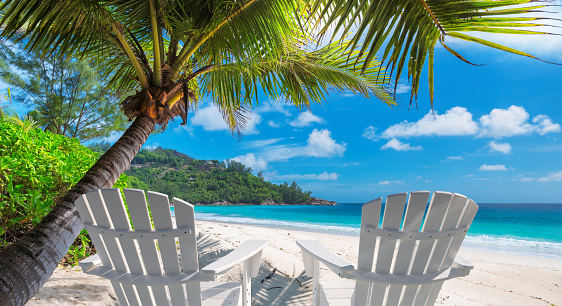 Beach chairs on sandy beach with palm and turquoise sea. Summer vacation and travel concept.